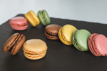 Colorful macaroons on a black slate stone served on a white table, Delicious French almond cookies, dessert.