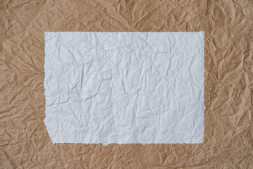 A rectangular blank sheet of crumpled paper lies on the same beige sheet. It looks like a frame with wide dark edges. Background. Texture.