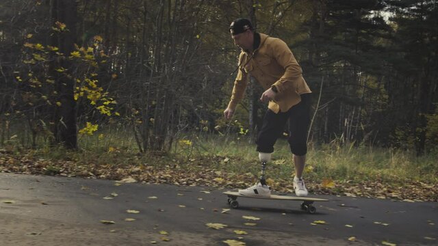 A young man with a metal prosthetic leg rides a skateboard in an autumn park. Go in for sports with an artificial leg. a11y