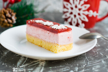 Delicious strawberry mousse cake with winter decor snowflakes on a white plate with a spoon, New Year's decor and a red cup with tea on the background.