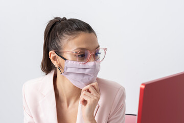 Salisbury, Wiltshire, UK. 2021. Attractive woman wearing pink face mask and looking at a computer screen.