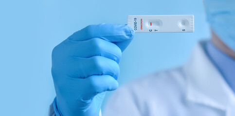 A doctor or nurse wearing a protective mask and gloves shows a rapid laboratory test for COVID-19 Omicron to detect IgM and IgG antibodies to the new coronavirus. The test shows a negative result.