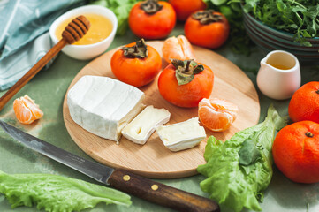 Ingredients and the process of making a vitamin winter salad with persimmons, tangerines and cheese. Selective focus