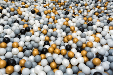 Many different color (white, gold, grey, black) plastic balls in ball pool at indoors playground