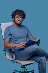 Tranquil guy in eyeglasses posing for the camera during reading