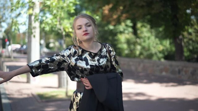 Young elegant slim woman hitchhiking at urban road outdoors in the morning. Portrait of beautiful Caucasian lady on sunny summer day at park soliciting a ride. Lifestyle concept
