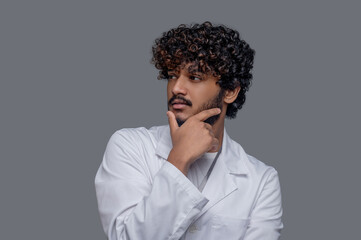 Obraz premium Pensive dark-haired young practitioner in a lab coat looking away