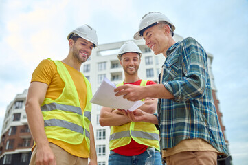 Naklejka premium Three men with drawing discussing at construction site