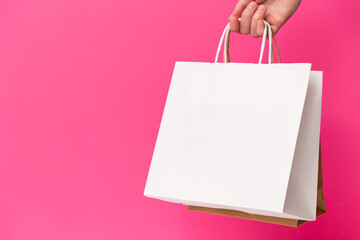 Female hand holding two shopping bags isolated on pink background. White and brown craft blank...