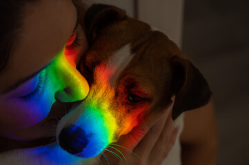 Close-up portrait of a woman hugging a jack russell terrier dog with a ray of rainbow light on her...