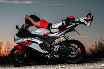 sexy young woman lying on her back on her road motorcycle dressed in protective pants and black...