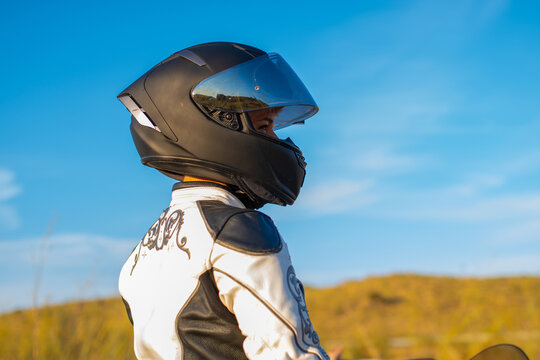 young biker woman in profile dressed in white patterned jacket and black safety helmet. blue sky background