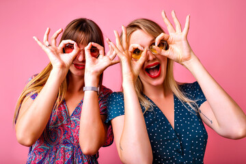 Studio portrait of two positive best friend women having fun at pink background