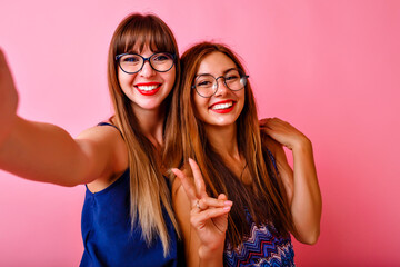 Two exited pretty women posing at pink background