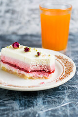 Cutaway sweet mousse cake on vintage plate and glass of multifruit juice on gray background with copy space