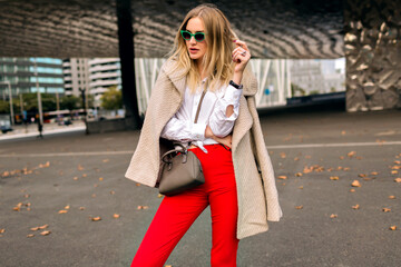 Trendy autumn fashion portrait of stylish young woman posing near modern architecture
