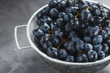 Sweet black grapes in a metal bowl on a dark textured background.