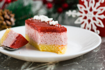 Appetizing slice of delicious fruit mousse cake on spoon close up, brownie on white plate, cup and christmas decor on background