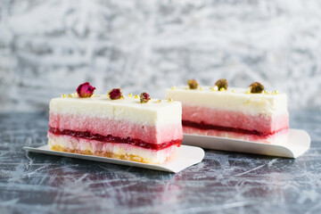 Two delicious mousse cakes with decorative roses on a gray background side view.