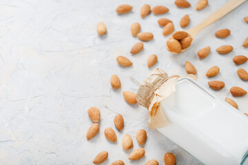 Almond milk in a glass bottle on a light background with a scattering of seed kernels and a wooden spoon.