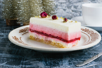 Fruit mousse cake on vintage plate, cup of coffee and decorative christmas tree on gray background.