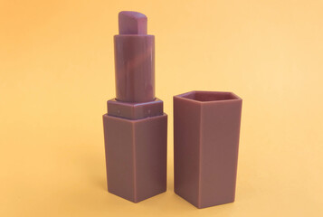 matte lipstick on an orange matte background. beige lipstick in the shape of a heart, soft brown shade. nude lip makeup