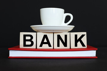 BANK. text on wooden cubes. On a black background. red notepad. a cup of coffee on cubes