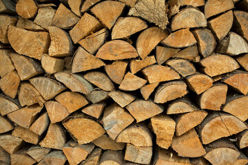 Background of dry chopped firewood logs in a pile. Wall of firewood. Alternative fuel concept.