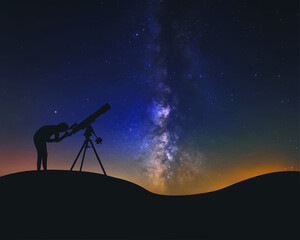 A man at night looks through a telescope refractor at the stars and the Milky Way 