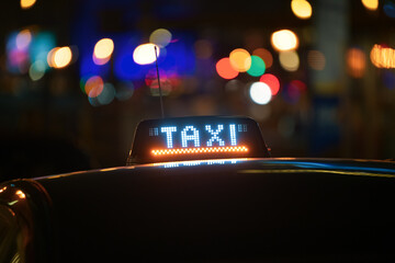 Taxi sign on top of a taximetre car in Brussels, Belgium. Photo shot during the night with city lights in background.