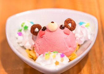 Close up on a Japanese strawberry ice cream and cheerios shaped as a cute bear character topped with sweet whipped cream and colorful sugar decorations on corn flakes.
