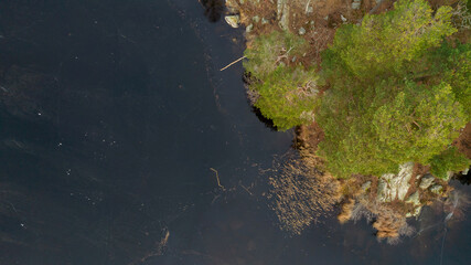 Beautiful Scandinavian landscape photographed with a drone on a sunny late autumn or winter day. Island with evergreen trees in the middle of frozen lake.