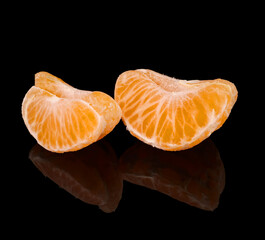 Slices of ripe tangerine, on a black background, with reflection