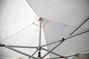 An iron structure supporting the tarpaulin canopy. A metal structure of various rails and joints holds a white tarpaulin awning in the form of quadrangular primaids.