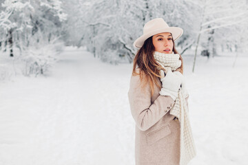 Winter female fashion. Portrait of stylish young woman in snowy winter park wearing white and beige...
