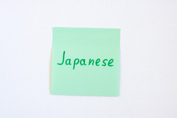 Top view flat lay of the reminder notepaper of green color with word Japanese on it on white background. Flashcards and language studies concept