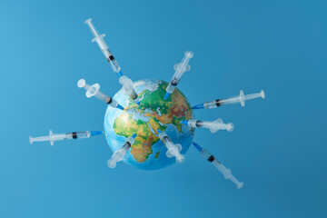 A globe studded with a lot of syringes with a vaccine on a light blue background. Copy space.