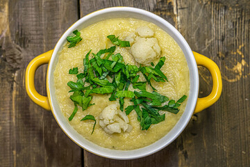 homemade dietary mashed cauliflower in ceramic bowl seasoned with parsley on a wooden table