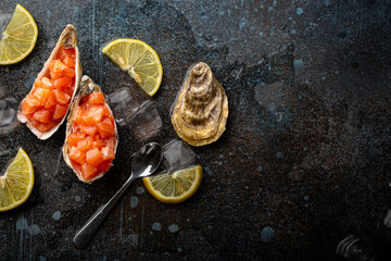 Delicious salmon tartare raw chopped in cubes served in oyster shells with lemon wedges and ice on blue stone rustic background, seafood appetizer or starter top view 