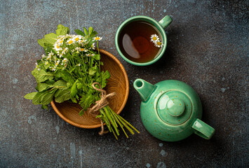 Herbal tea with fresh medical herbs and flowers, tea cup, tea pot and bouquet of fresh wild flowers and healing herbs top view on stone background, herbal alternative medicine and homeopathy 