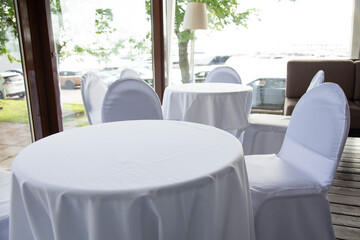 interior with white tables and chairs in a cafe restaurant under white tablecloths
