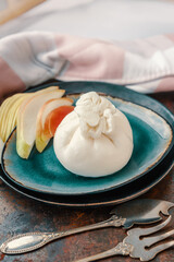 Burrata Buffalo cheese with pear. Traditional Italian, fresh, soft white cheese burrata ball of mozzarella and cream on a round dark plate, with slices of pear on a dark background