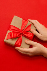 children's hands hold a gift wrapped in kraft paper and with a red ribbon on a red background
