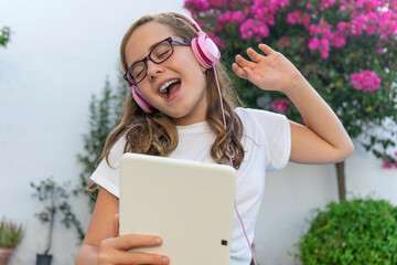 GIRL WITH GLASSES AND EYES CLOSED LISTENING TO MUSIC AND SINGING OUTDOOR WITH TABLET AND PINK...