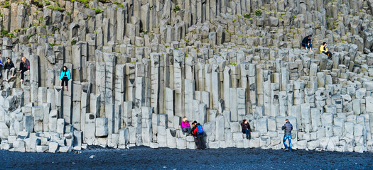 Tourists sitting on basalt rocks at Black Beach, Reynisfjara, Vik, Iceland