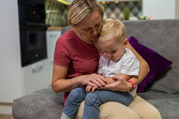 little boy sits sad on mom's knees, his hand hurts