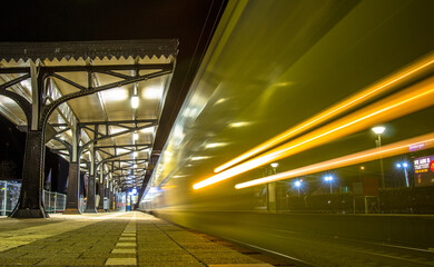 Night Photography with the Motion blur of a Yellow Dutch NS train, taken from a low perspective on the platform, under the a historical  platform roof..