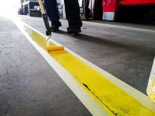 Closeup of a person painting a yellow line on a garage floor under the lights