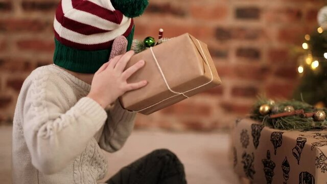 A curious boy takes Christmas presents from under the tree, shakes it, tries to find out what's inside. Happy christmas for baby