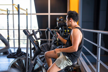 Fototapeta na wymiar Young man cheking his phone while he is on a cycling machine in the gym